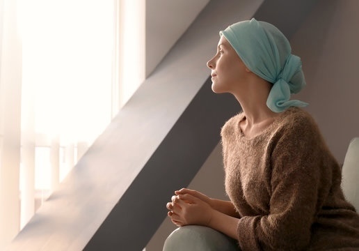 Young woman with cancer, wearing a head scarf and looking out of the window.
